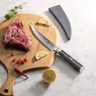 
                    
                      6-inch boning knife with polished handle and sheath next to raw meat, lemon slices, chili, and herbs on wooden board.
                    
                  