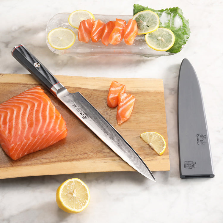 8-inch sashimi knife with black handle on wooden board next to sliced salmon and lemon wedges, knife sheath nearby.