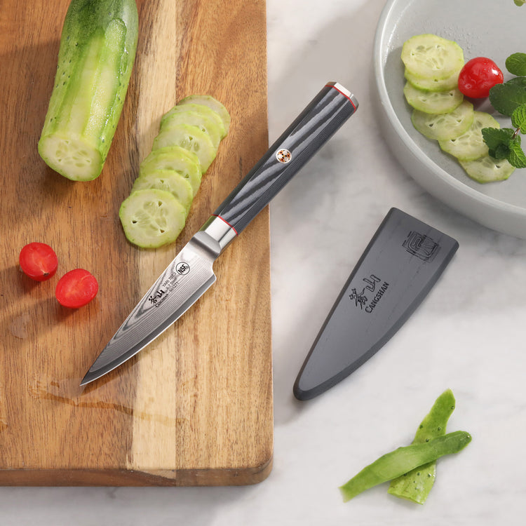 3.5-inch paring knife with Damascus steel blade and black handle on cutting board with sliced cucumber and cherry tomatoes, s