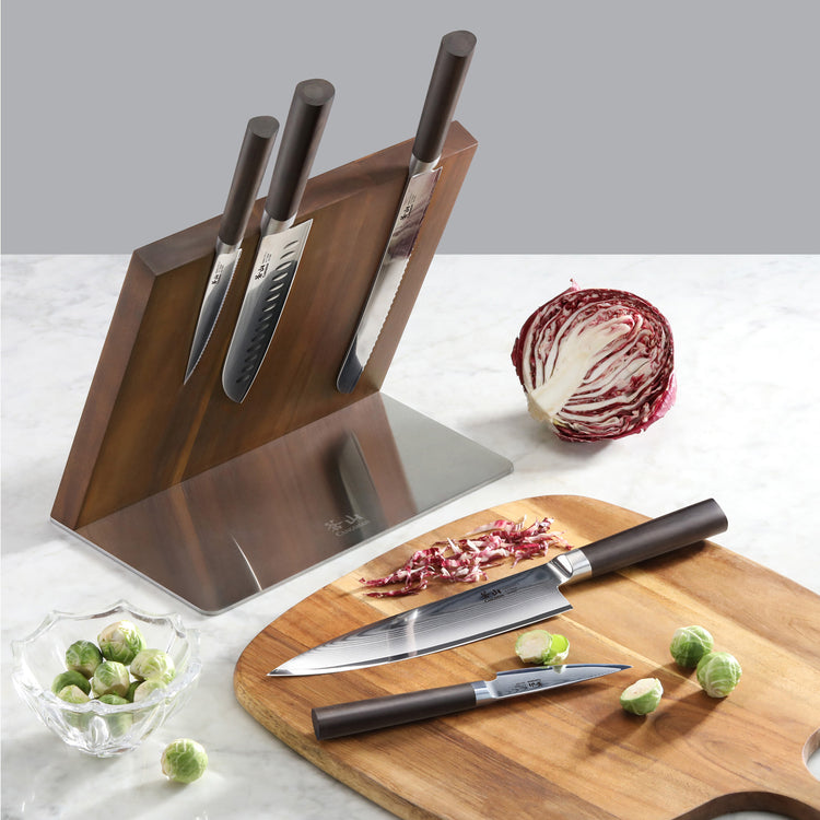 Six-piece knife set with three knives magnetically attached to a wooden block, two knives on a cutting board, Brussels sprout
