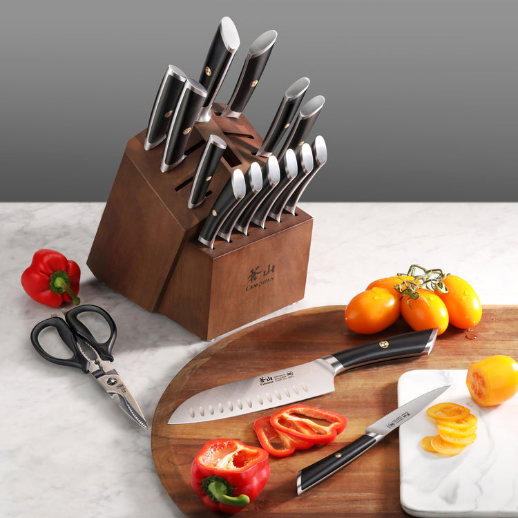 Wooden knife block with knives and steak knives, kitchen scissors, sliced red bell pepper, and yellow tomatoes on cutting boa