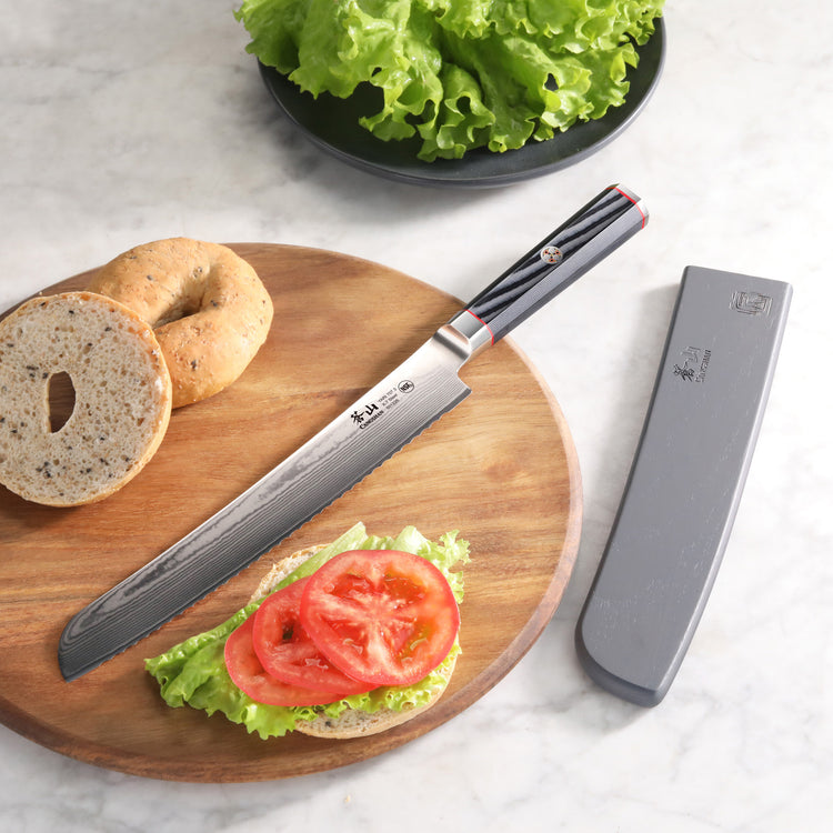 9-inch bread knife with Damascus steel blade and black handle on wooden board with sliced bagel, lettuce, tomato, and sheath.
