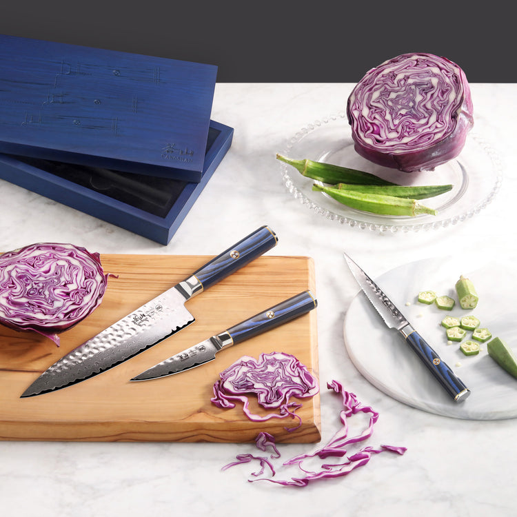 Three knives with blue handles on a wooden board and marble plate, alongside sliced purple cabbage and okra.