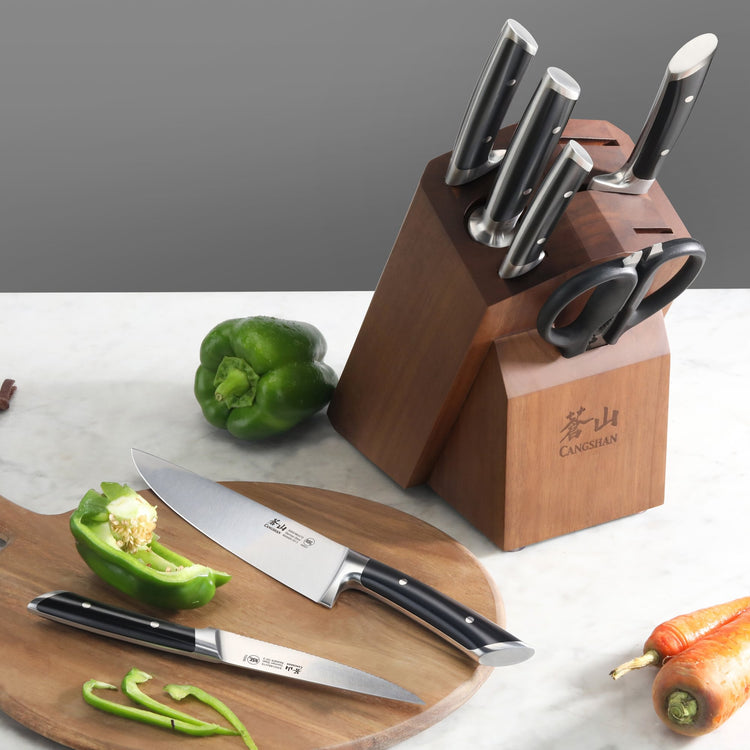 Knife block set with six knives and scissors, two knives on a cutting board with sliced green bell pepper.