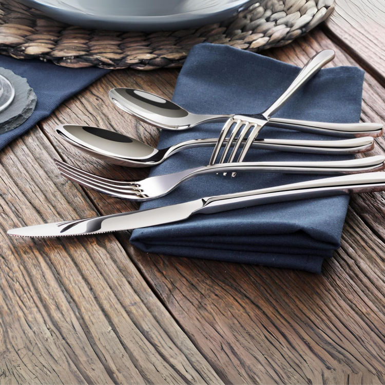 Four stainless steel flatware pieces—a knife, fork, tablespoon, and teaspoon—rest on a folded navy napkin.