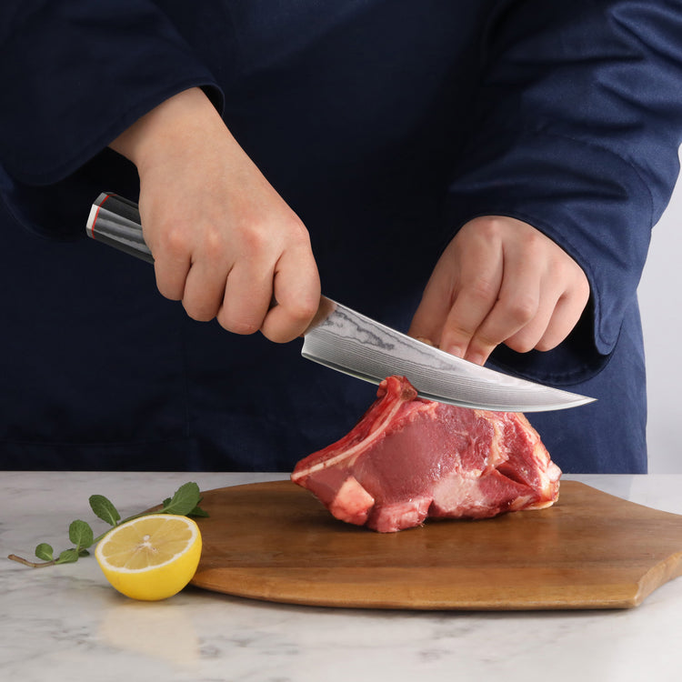 Person slicing raw meat on wooden cutting board with a 6-inch boning knife and a lemon half nearby.