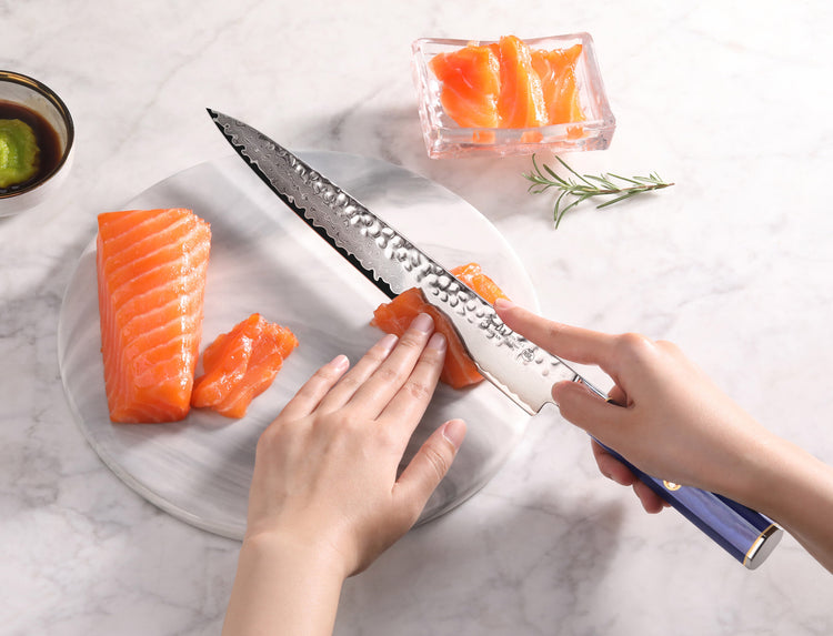 Hands slicing fresh salmon with a 10-inch sashimi knife featuring a blue handle and hammered blade texture.