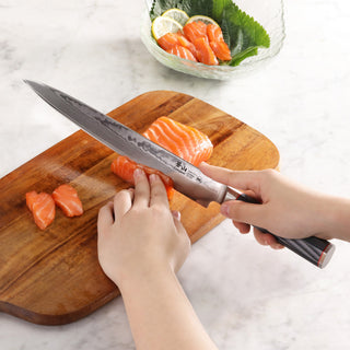 
                    
                      Hands slicing raw salmon on a wooden board with a 10-inch sashimi knife featuring a patterned blade and dark handle.
                    
                  
