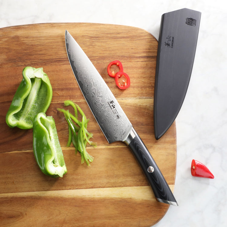 8-inch chef's knife with patterned blade and black handle on wooden board with sliced green and red peppers and black sheath