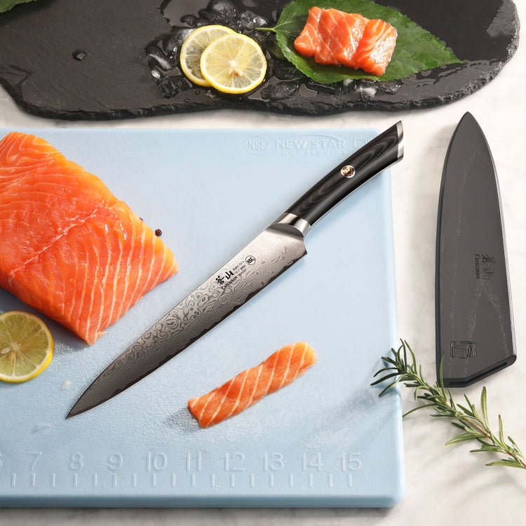 8-inch carving knife with Damascus steel blade slicing salmon on a blue cutting board with lemon and herbs nearby.