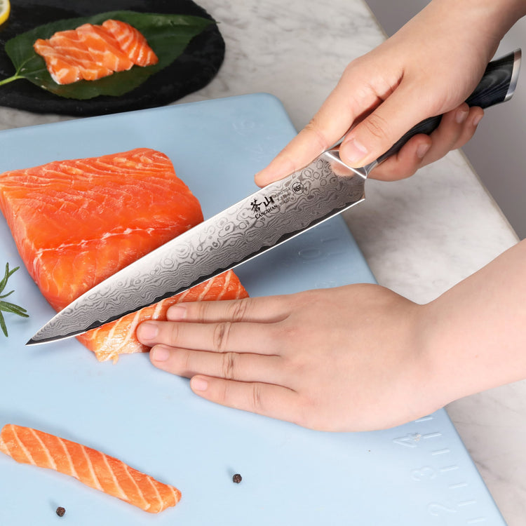 Hand slicing fresh salmon on a blue cutting board using a patterned high-carbon steel knife.