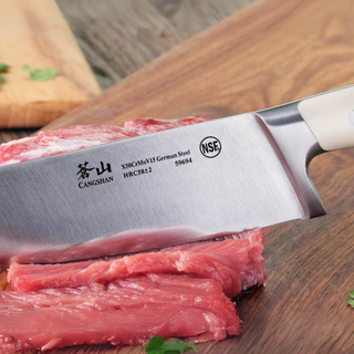 
                    
                      Close-up of a Cangshan kitchen knife slicing raw meat on a wooden cutting board.
                    
                  