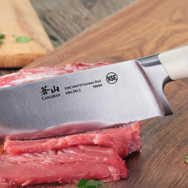 Close-up of a Cangshan kitchen knife slicing raw meat on a wooden cutting board.