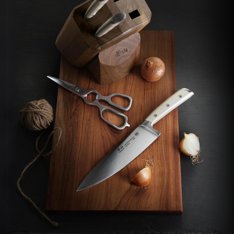 Chef knife, kitchen shears, onions, and a wooden knife block on a wooden cutting board.