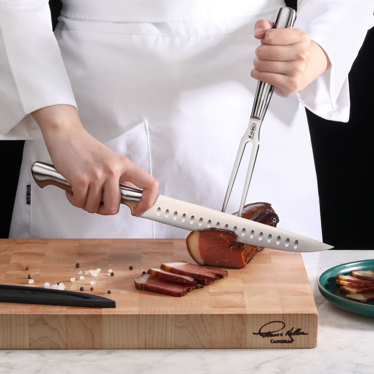 Person carving cooked meat on a wooden cutting board using a carving knife and fork with stainless steel handles.