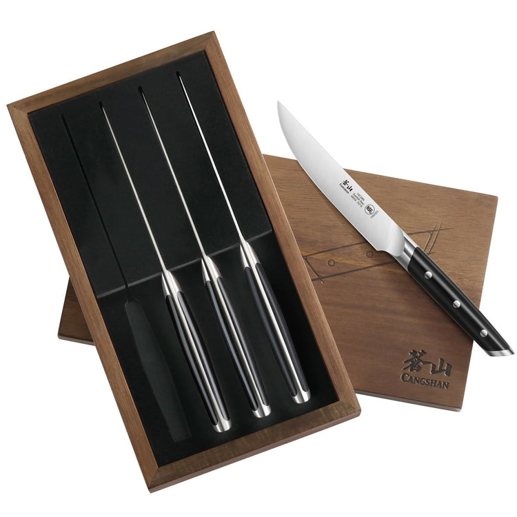 Four stainless steel steak knives with black handles in a wooden box, one knife resting on the box lid.