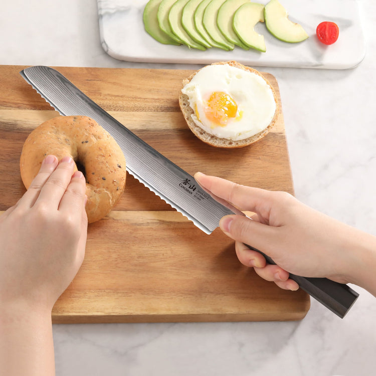 A person slicing a bagel on a cutting board with the MAYA Series 9-Inch Bread Knife, X-7 Damascus Steel.