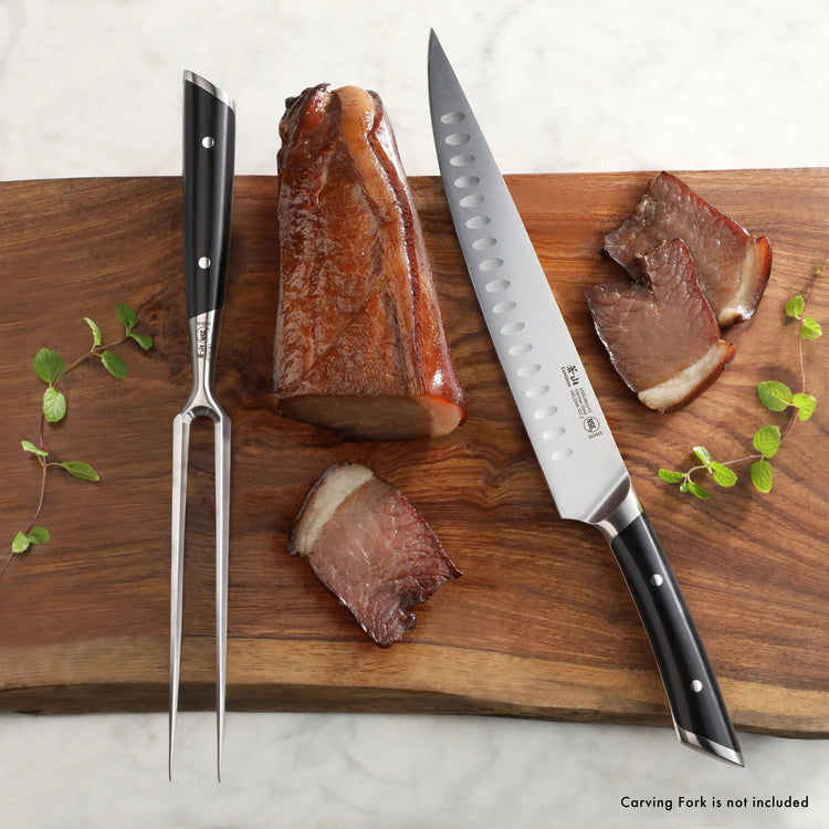 9-inch carving knife with black handle and hollow edge blade next to sliced roast beef and a two-prong fork on wooden board