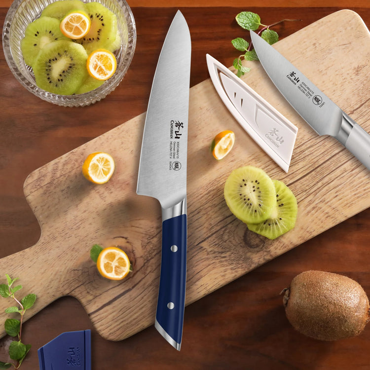 Two kitchen knives with navy and white handles on a wooden cutting board with sliced kiwi and kumquats.