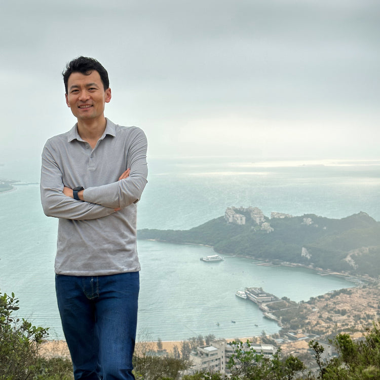Henry Liu standing with arms crossed on a hilltop overlooking a coastal bay.