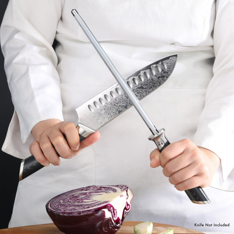 Person holding a honing steel and a chef's knife above a halved red cabbage on a wooden surface.