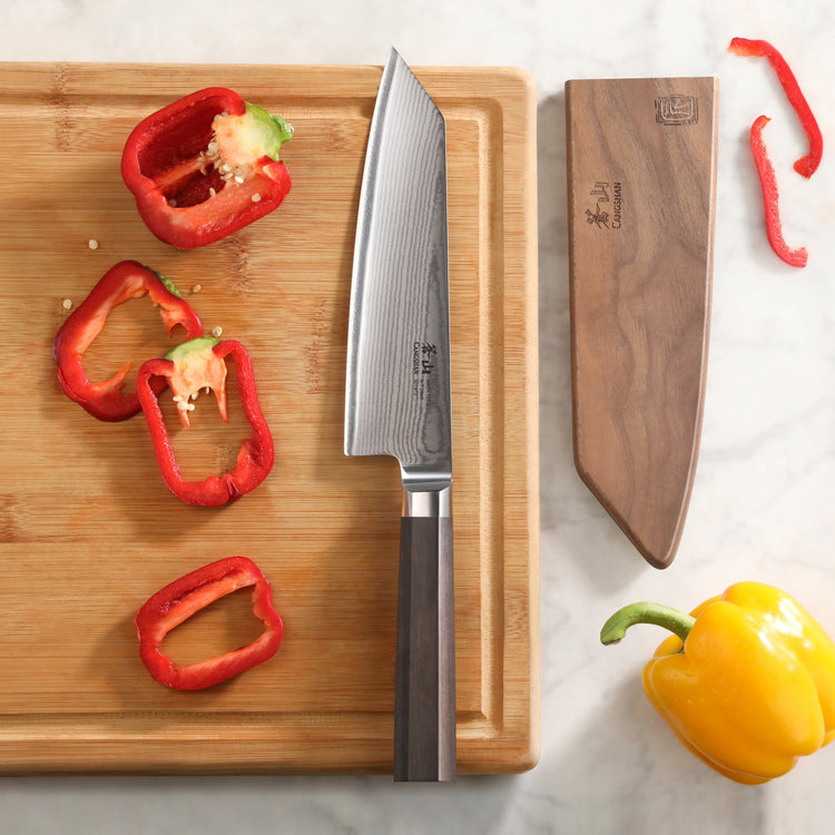 MAYA Series 7-Inch Kiritsuke Knife X-7 Damascus Steel on a wooden cutting board beside its wooden sheath.