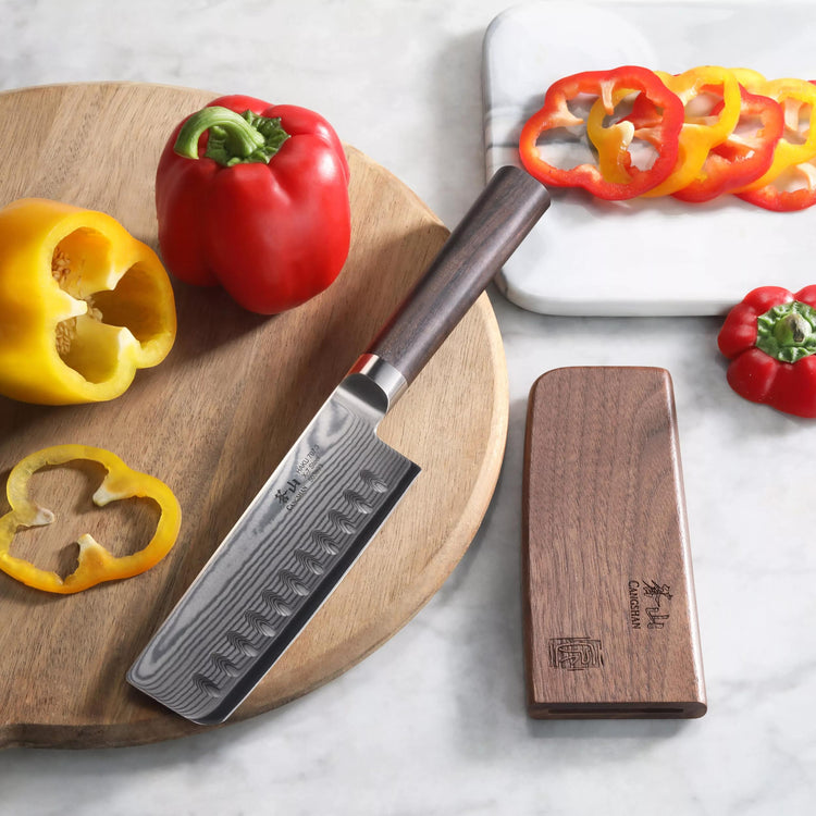 Nakiri knife with wooden handle and sheath on a cutting board with sliced red and yellow bell peppers.