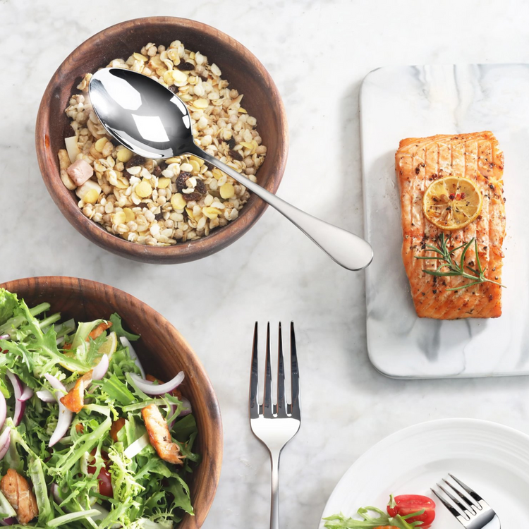 Serving spoon with matte finish handle resting in a wooden bowl of grain salad on a marble surface.
