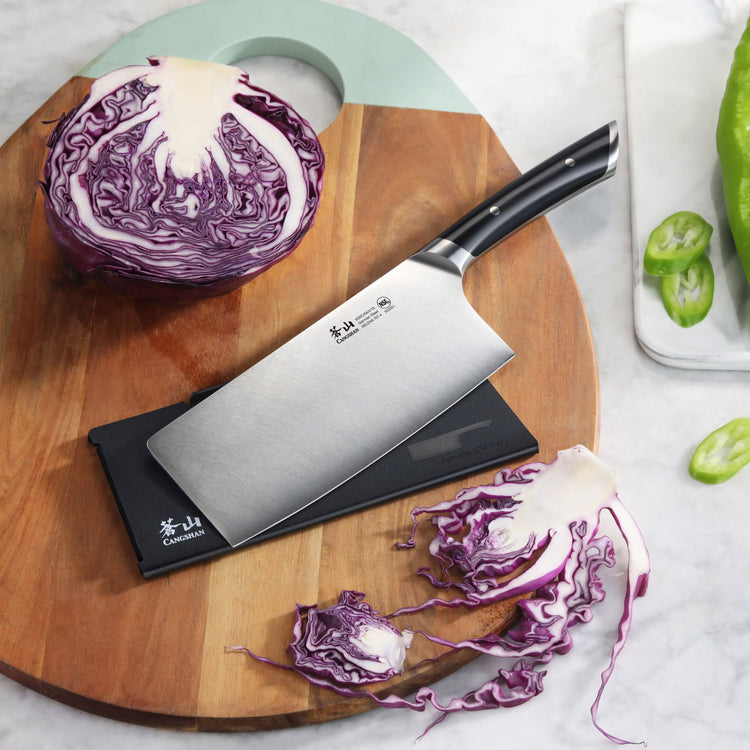 7-inch vegetable cleaver with black handle on wooden board, next to halved and shredded purple cabbage.