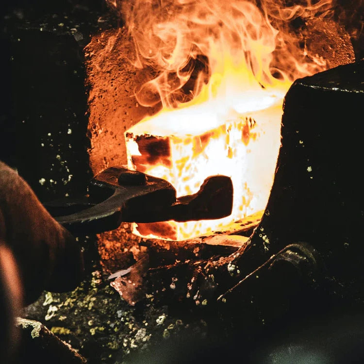 Blacksmith tongs holding a glowing hot steel block inside a fiery forge.
