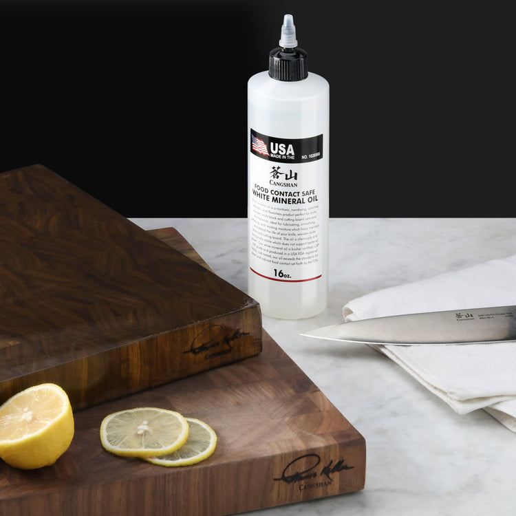 Bottle of white mineral oil for blade protection standing on a marble surface next to wooden cutting boards, lemon slices, an