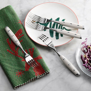 
                    
                      Four stainless steel steak forks with white handles arranged on a plate and green napkin on a marble surface.
                    
                  