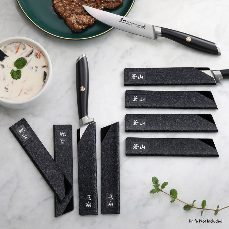 Eight black textured knife guards of varying sizes arranged on a marble surface, with one guard partially covering a steak kn