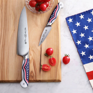 
                    
                      Two knives with American flag design handles on a wooden cutting board, next to halved cherry tomatoes and a star-patterned c
                    
                  