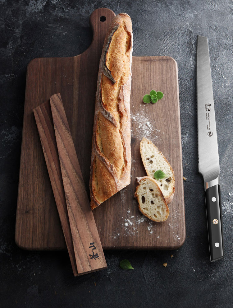 Solid ash wood magnetic knife sheath resting on a wooden cutting board with a baguette and sliced bread.