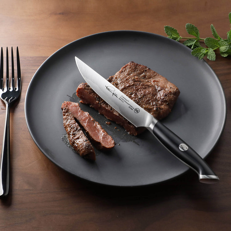 Steak sliced on a black plate with a black-handled fine-edge steak knife resting on the plate.