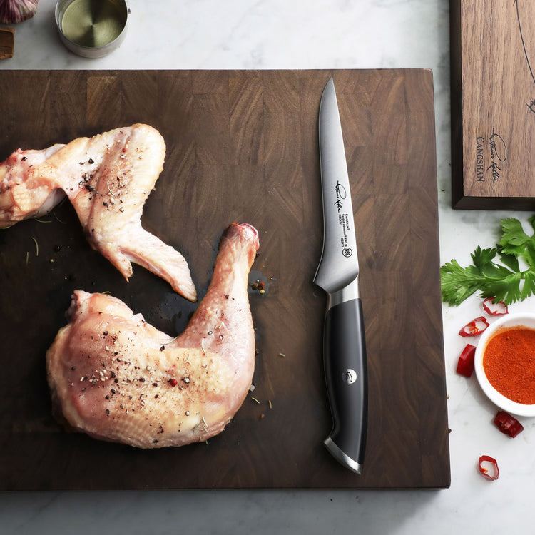 Boning knife with black handle on wooden board next to seasoned raw chicken leg and wing.