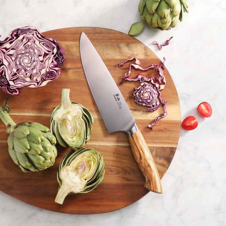 8-inch chef's knife with olivewood handle on wooden board with artichokes, cabbage, and cherry tomatoes.