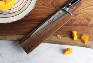 
                    
                      Magnetic knife sheath made of solid ash wood holding a kitchen knife on a wooden cutting board with pumpkin pieces nearby.
                    
                  