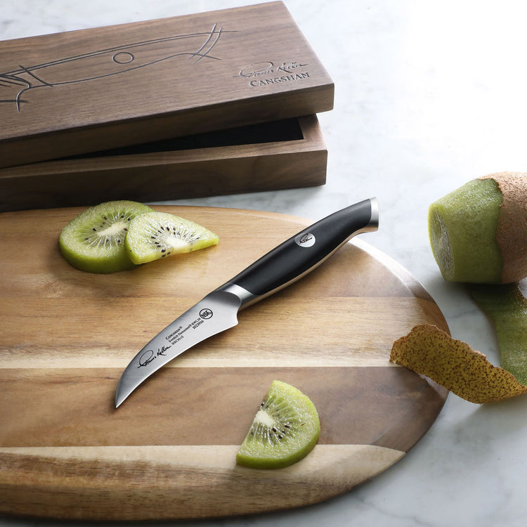 Small curved peeling knife with black handle on wooden cutting board next to sliced kiwi and kiwi peel.