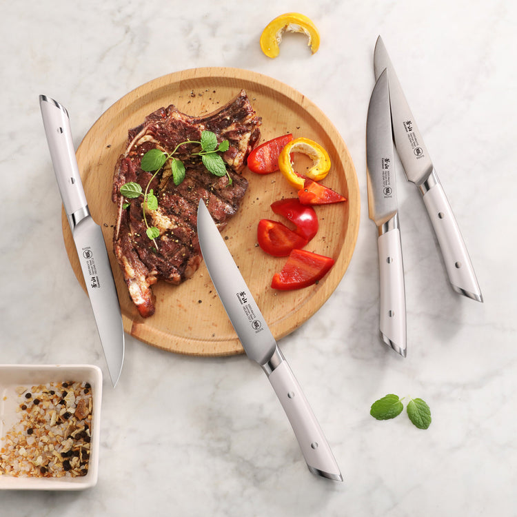 Four stainless steel steak knives arranged around a wooden plate with grilled steak, red and yellow bell pepper slices, and h