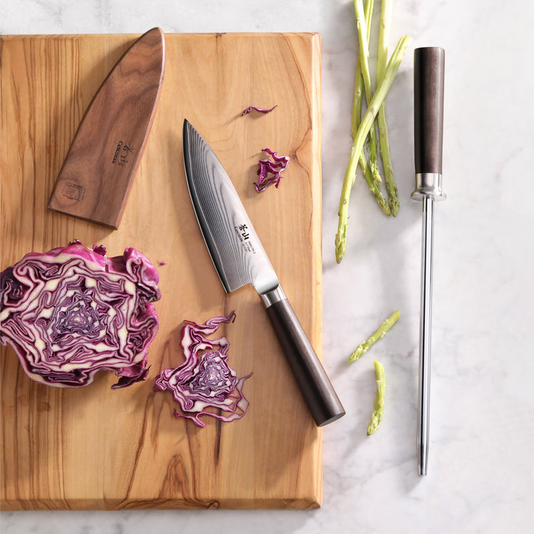 HAKU Series High-Carbon 9-inch honing steel with dark wooden handle next to a chef's knife, wooden sheath, and cut purple cab
