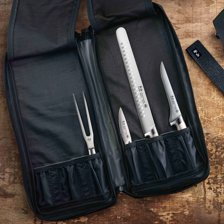 Open black nylon knife bag with four knives and a carving fork secured inside, displayed on a wooden surface.