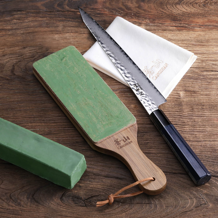 Leather paddle strop with green compound bar, serrated knife, and white cloth on wooden surface.