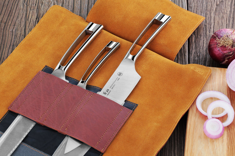 Four silver knives with curved handles in a brown leather roll-up case on a wooden surface next to sliced onions.