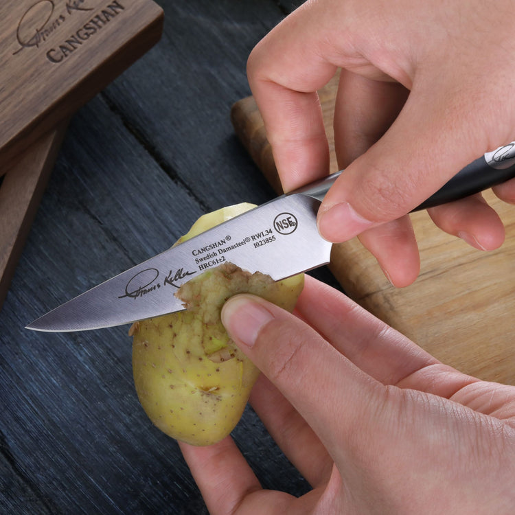 Hand holding a small knife peeling the skin off a yellow potato over a wooden cutting board.