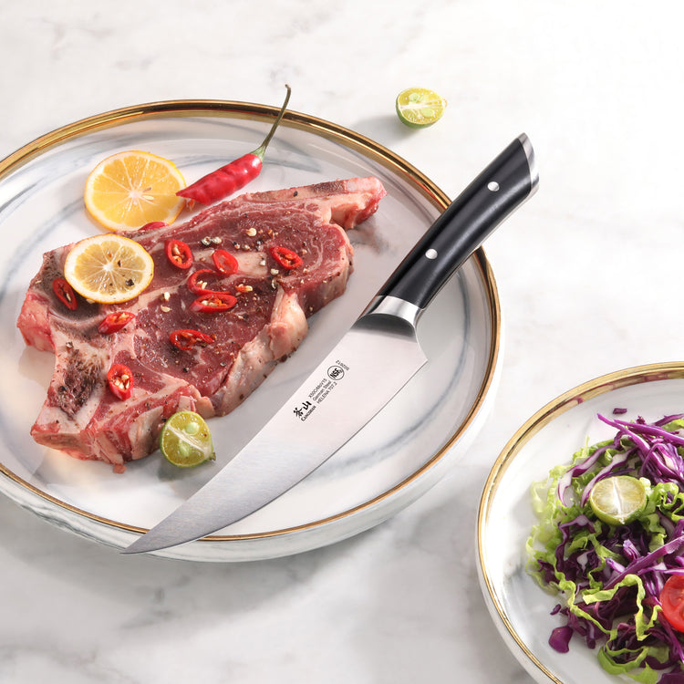 6-inch boning knife with black handle on a plate next to seasoned raw steak, lemon slices, chili, and lime wedges.