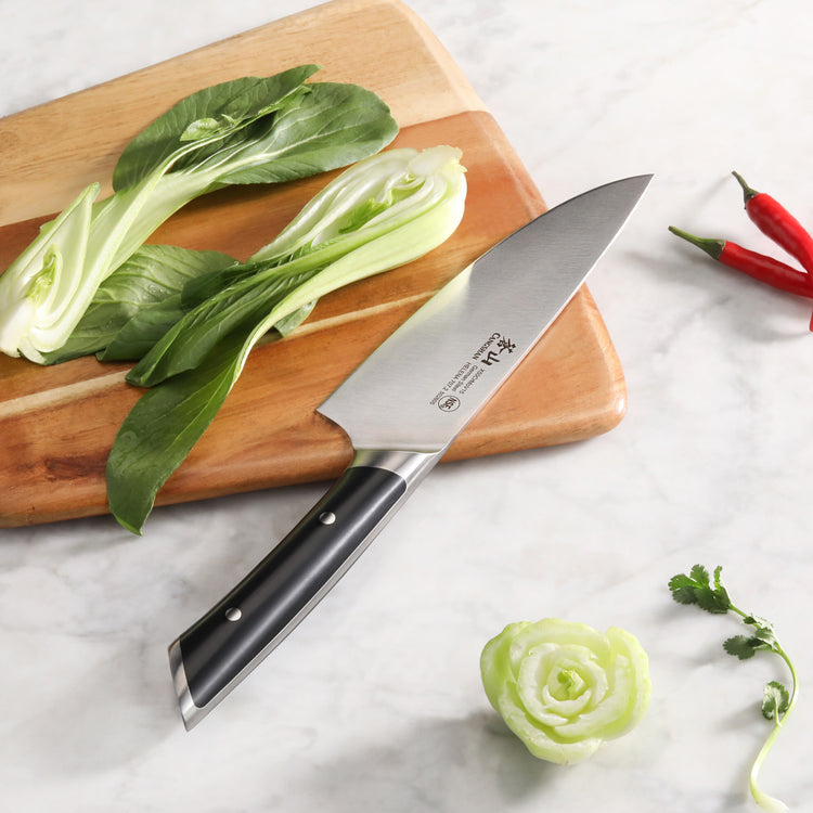 8-inch chef's knife with black handle on a wooden cutting board next to chopped bok choy and chili peppers.