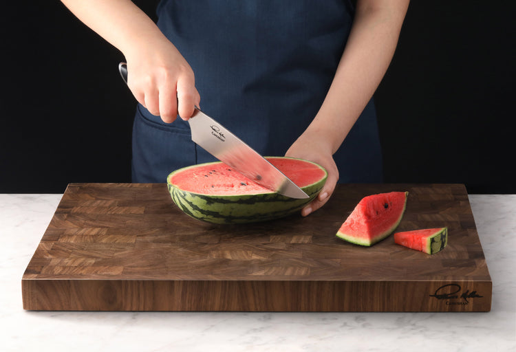 Person slicing a watermelon on a thick wooden end-grain cutting board with a chef's knife.