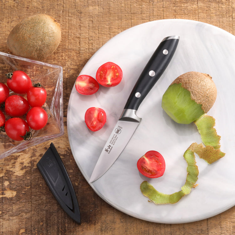 3.5-inch paring knife with black handle on white cutting board, surrounded by peeled kiwi and halved cherry tomatoes.